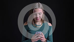 Portrait of young brunette caucasian girl laughing watching into smartphone on black background.