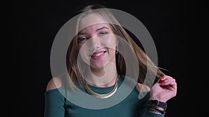 Portrait of young brunette caucasian girl smiling into camera and fixing her hair flirtingly on black background.