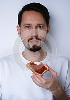 Portrait of a young brunette man eating toast with jam on a white background