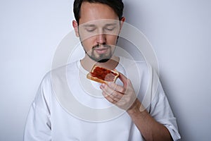 Portrait of a young brunette man eating toast with jam on a white background