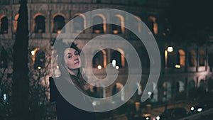 Portrait of young brunette woman standing near Colosseum in Rome, Italy in evening. Girl turns and looks at camera.