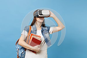 Portrait of young brunette woman student in denim clothes with backpack wearing virtual reality headset holding school