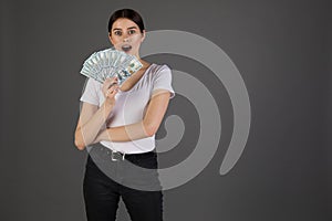 Portrait of young brunette woman in whote t-shirt holding money banknotes and celebrating