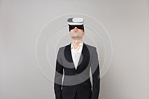 Portrait of young business man in classic black suit and white shirt looking up in headset isolated on grey wall