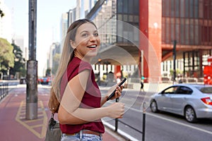 Portrait of young business woman holding smartphone looking away on Paulista Avenue, Sao Paulo, Brazil
