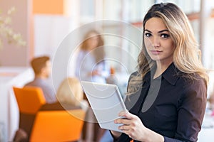 Portrait of young business woman at modern startup office interior, team in meeting in background