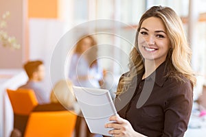 Portrait of young business woman at modern startup office interior, team in meeting in background