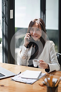 Portrait of young business woman sitting in front of her laptop and talking on mobile phone.