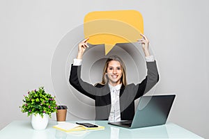 Portrait of a young business woman sitting at the office desk with empty speech bubbles above her head