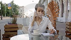 Portrait of young business woman sitting relaxed at outdoor cafe drinking coffee and calling her cell phone