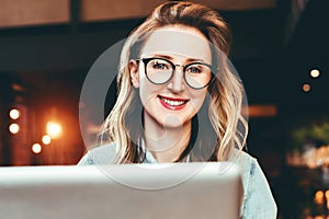 Portrait of young business woman in trendy glasses sitting in cafe,working on laptop.Blogger communicates with followers