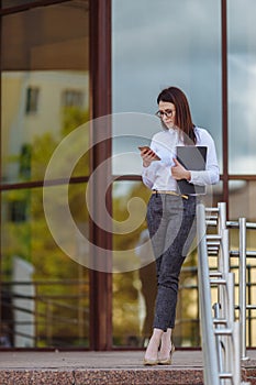 Portrait young business woman wearing white shirt using smartphone out doors. Female reading sms message in working