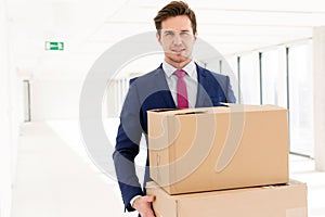 Portrait of young businessman carrying cardboard boxes in new office