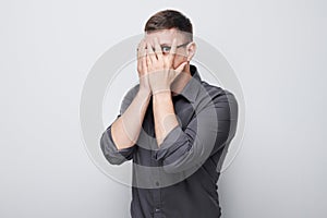 Portrait of young businessman covering eyes with hand, peeking through fingers