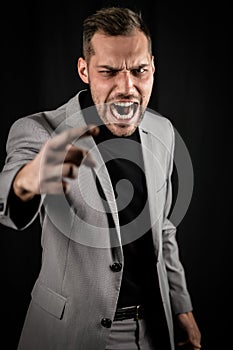 Portrait of a young businessman in a gray suit, very angry yelling and gesturing accusingly in front of him