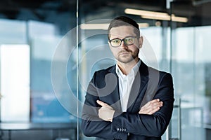 Portrait of a young businessman, a lawyer in a suit and glasses standing in the office, crossing his arms on his chest