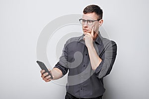 Portrait of young businessman looks on mobile phone and thinks. Person with smartphone