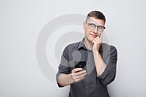 Portrait of young businessman looks on mobile phone and thinks. Person with smartphone