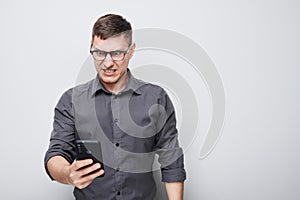 Portrait of young businessman looks on mobile phone and thinks. Person with smartphone