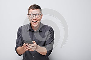 Portrait of young businessman with mobile phone in hand celebrates victory, winning money in casino. Person with smartphone