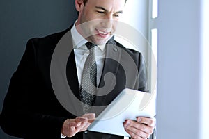 Portrait of young businessman in office with big window. Businessman using tablet computer and looking at camera