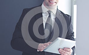 Portrait of young businessman in office with big window. Businessman using tablet computer and looking at camera.