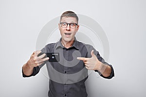 Portrait of young businessman showing blank mobile phone screen with excited face. Person with smartphone