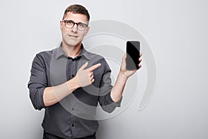 Portrait of young businessman showing blank mobile phone screen with excited face. Person with smartphone