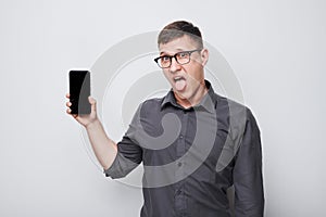 Portrait of young businessman showing blank mobile phone screen with excited face. Person with smartphone