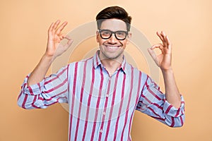 Portrait of young businessman showing double okay sign gesturing his good feedback to your job results isolated on beige