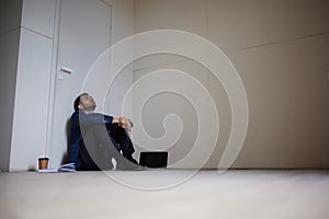 Portrait of young businessman sitting on floor in empty room. Business closure. Depression and crisis. Losing job and