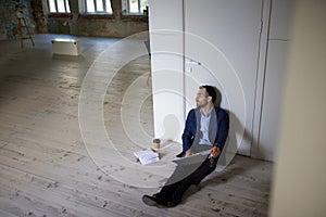 Portrait of young businessman sitting on floor in empty room. Business opening. Working on new company projects