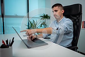 Portrait of young businessman sitting and pointing finger at his computer screen