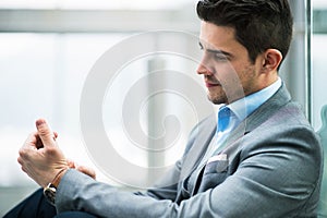 A portrait of young businessman with smartphone sitting in corridor outside office.