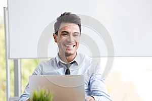 Portrait of young businessman smiling and working with laptop at office,