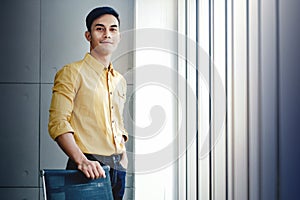 Portrait of Young Businessman Standing by the Window in Office. Looking at Camera and Smiling. Happy Person