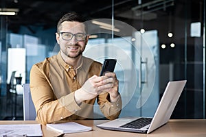 Portrait of a young businessman working in an office center, sitting at a desk and using a mobile phone. Smiling looking