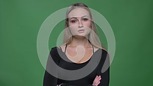 Portrait of young businesswoman in black blouse watching into camera interrogatively at green background.