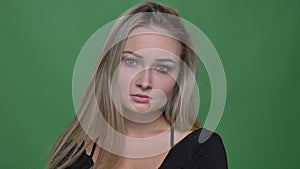 Portrait of young businesswoman in black blouse watching seriously and fixedly into camera at green background.