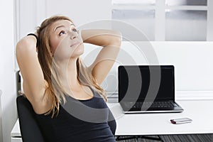 Portrait of young businesswoman with hands behind head sitting in front of desk in office