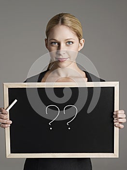 Portrait of young businesswoman holding blackboard with question marks
