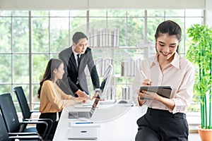 Portrait of young businesswoman looking at business document in tablet while her colleagues working in office background on