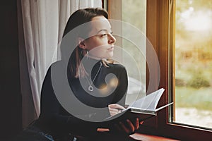 Portrait of young businesswoman with notebook and phone at window