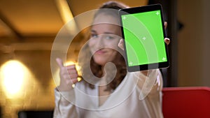 Portrait of young businesswoman showing green screen of tablet with recommendation of the app on office background. photo