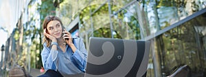 Portrait of young businesswoman sitting outside in park, talking on mobile phone, using laptop. Young woman, student