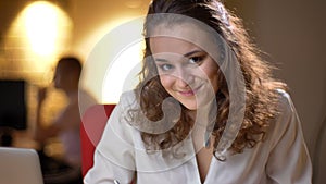 Portrait of young businesswoman watching smilingly and shyly into camera on office background. photo