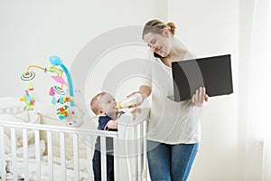 Portrait of young busy businesswoman working on computer, talking by phone and feeding her baby son