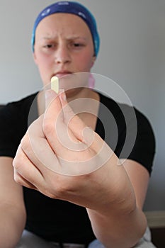 Portrait of a young cancer patient in a headscarf frowns at pill in foreground