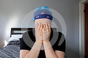 Portrait of a young cancer patient in a headscarf holds head in hands in distress