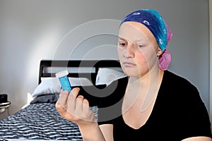 Portrait of a young cancer patient in a headscarf looks away from bottle of pills she is holding